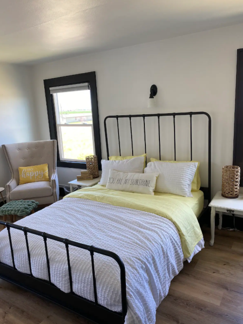 Cozy bedroom featuring a yellow and white bed, a comfy chair, and decorative accents in a bright, airy space.